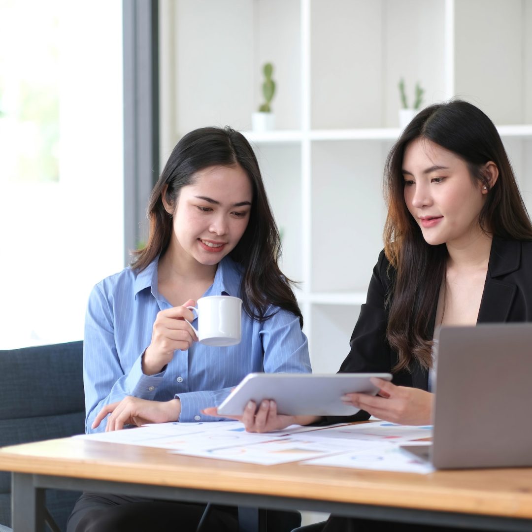 Two young Asian businesswoman discuss investment project working and planning strategy.